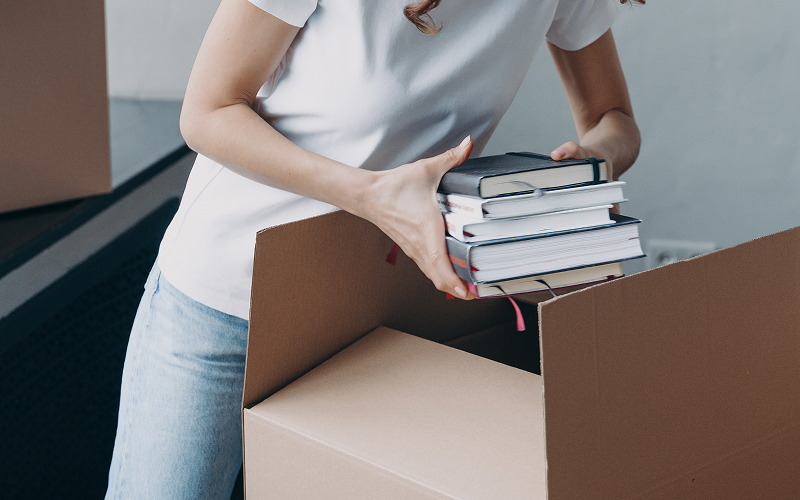 Person packing books into cardboard box without causing damage.