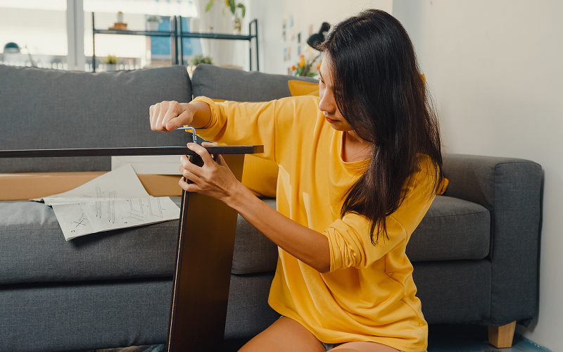 Woman using a tool to dismantle furniture before moving.