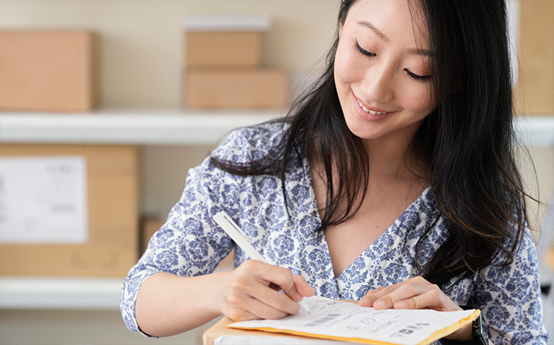 Smiling woman writing on a shipping label on cardboard package.