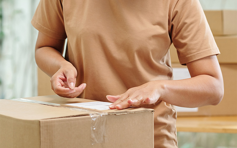 Close-up of a person placing a shipping label on a cardboard box.