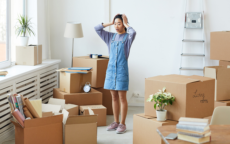 Stressed woman standing among moving boxes during house relocation.